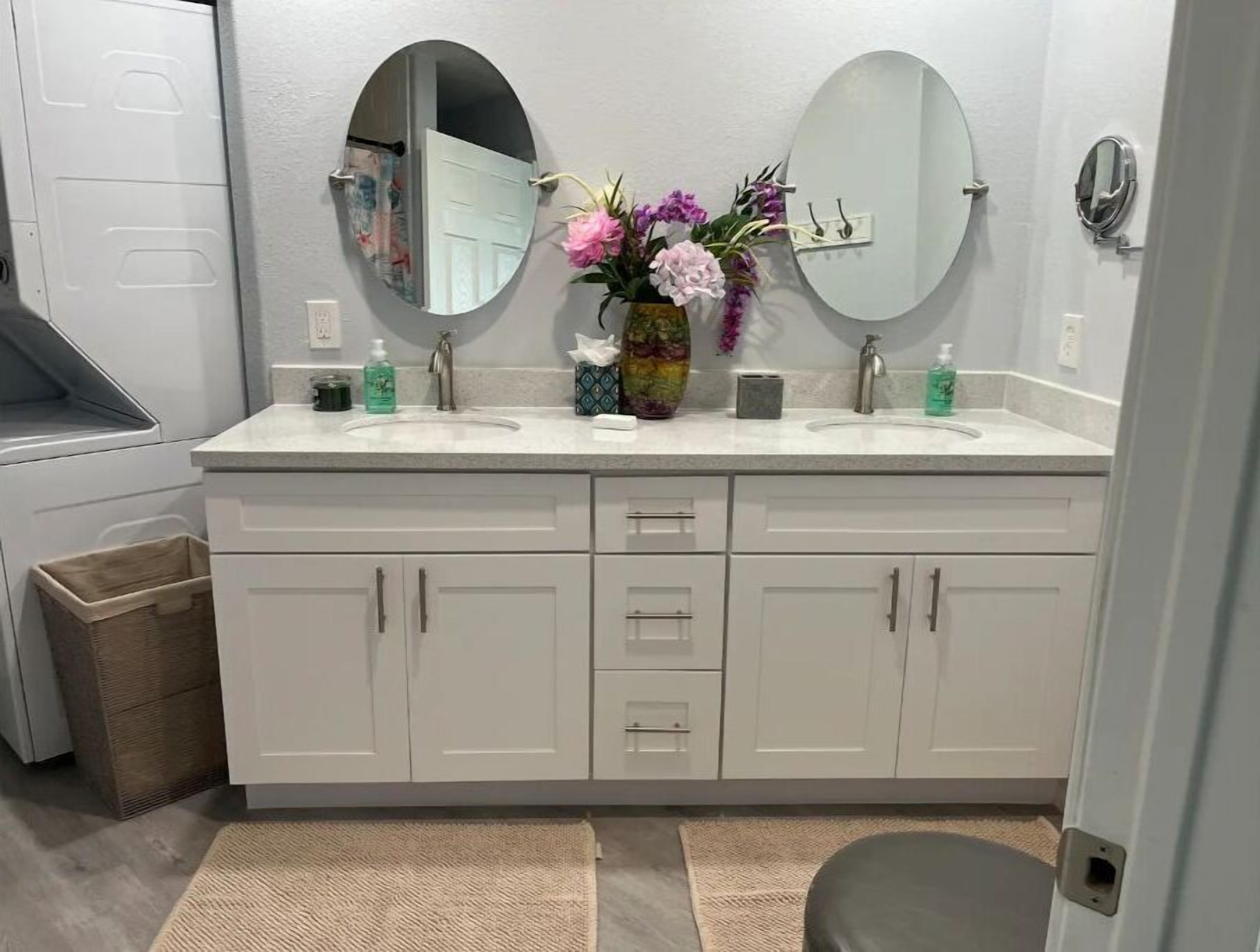 Un baño con dos lavamanos, un espejo y un jarrón con flores.