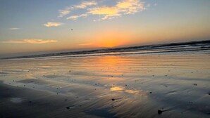 A beach at sunset with calm waves and a clear sky.