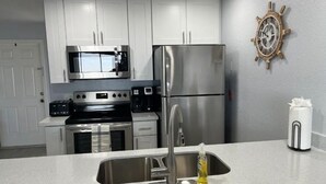 A modern kitchen with stainless steel appliances, white cabinets, and a ship's wheel decoration on the wall.