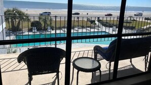 A balcony with a view of the beach, a swimming pool, and two chairs.