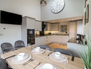 A modern kitchen with white cabinetry, a built-in oven, and a large wall clock. - Bryn Cae (Llandudno)