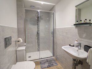 A modern bathroom with a glass-enclosed shower, a white sink, and a mirror above the sink. - Bryn Cae (Llandudno)