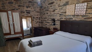 Een slaapkamer met een stenen muur, een houten garderobe, een bed met een witte dekbedovertrek en een nachtkastje met een lamp.