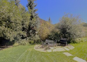 A patio with a table and chairs, surrounded by a grassy area and trees. - Bachman Village #9 - backyard and steps to skiing! (Telluride)