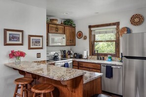 A kitchen with granite countertops, wooden cabinets, a stainless steel refrigerator, and a window with a view of greenery. - Bachman Village #9 - backyard and steps to skiing! (Telluride)
