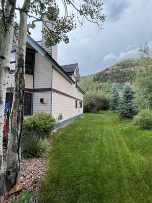 A house with a sloped roof, a well-maintained lawn, and a view of a forested hillside. - Bachman Village #9 - backyard and steps to skiing! (Telluride)