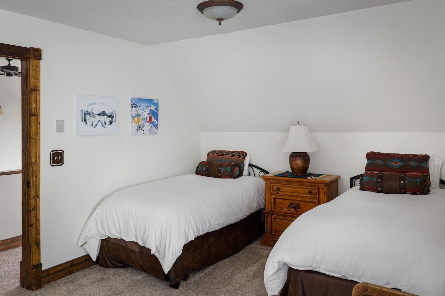 Une chambre avec deux lits simples, une commode en bois et une table de chevet avec une lampe.