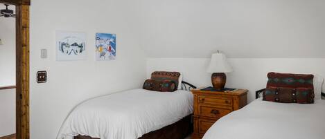 Une chambre avec deux lits simples, une commode en bois et une table de chevet avec une lampe.
