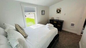 A bedroom with a bed, a dresser, and a window with blinds. - Modern Central Blackfoot Living (Blackfoot)
