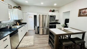 A modern kitchen with white cabinets, stainless steel appliances, and a dining area with a table and chairs. - Modern Central Blackfoot Living (Blackfoot)