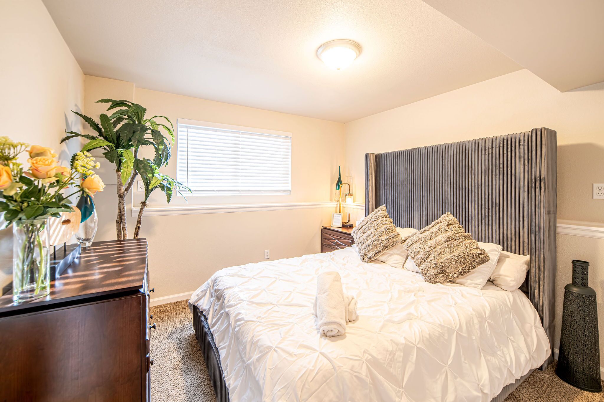 A bedroom with a bed, bedside table, lamp, and a window with blinds.