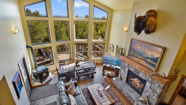 A spacious living room with a fireplace, large windows, and a stone fireplace surround. - Native Retreat Cabin (Summit County)