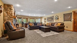 A spacious living room with a stone wall, a leather recliner, a dark brown sofa set, and a coffee table. - Native Retreat Cabin (Summit County)