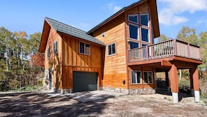 A two-story wooden house with a stone foundation, a garage, and a balcony. - Native Retreat Cabin (Summit County)