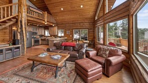 Un interior espacioso de cabaña de madera con cocina, comedor y una sala de estar acogedora con mobiliario de cuero y ventanas amplias.