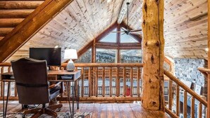 Un interior de madera con un escritorio, una silla y un ventanal que da a un paisaje nevado.
