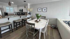 Une cuisine moderne avec des meubles blancs, un îlot central, des tabourets de bar et une table à manger avec des chaises.