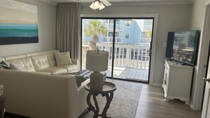 Un salon avec un canapé beige, une petite table ronde, un ventilateur de plafond et un téléviseur posé sur un meuble.