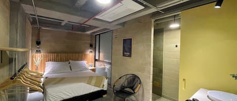Un dormitorio moderno con cama, una silla y baño con lavamanos e inodoro.