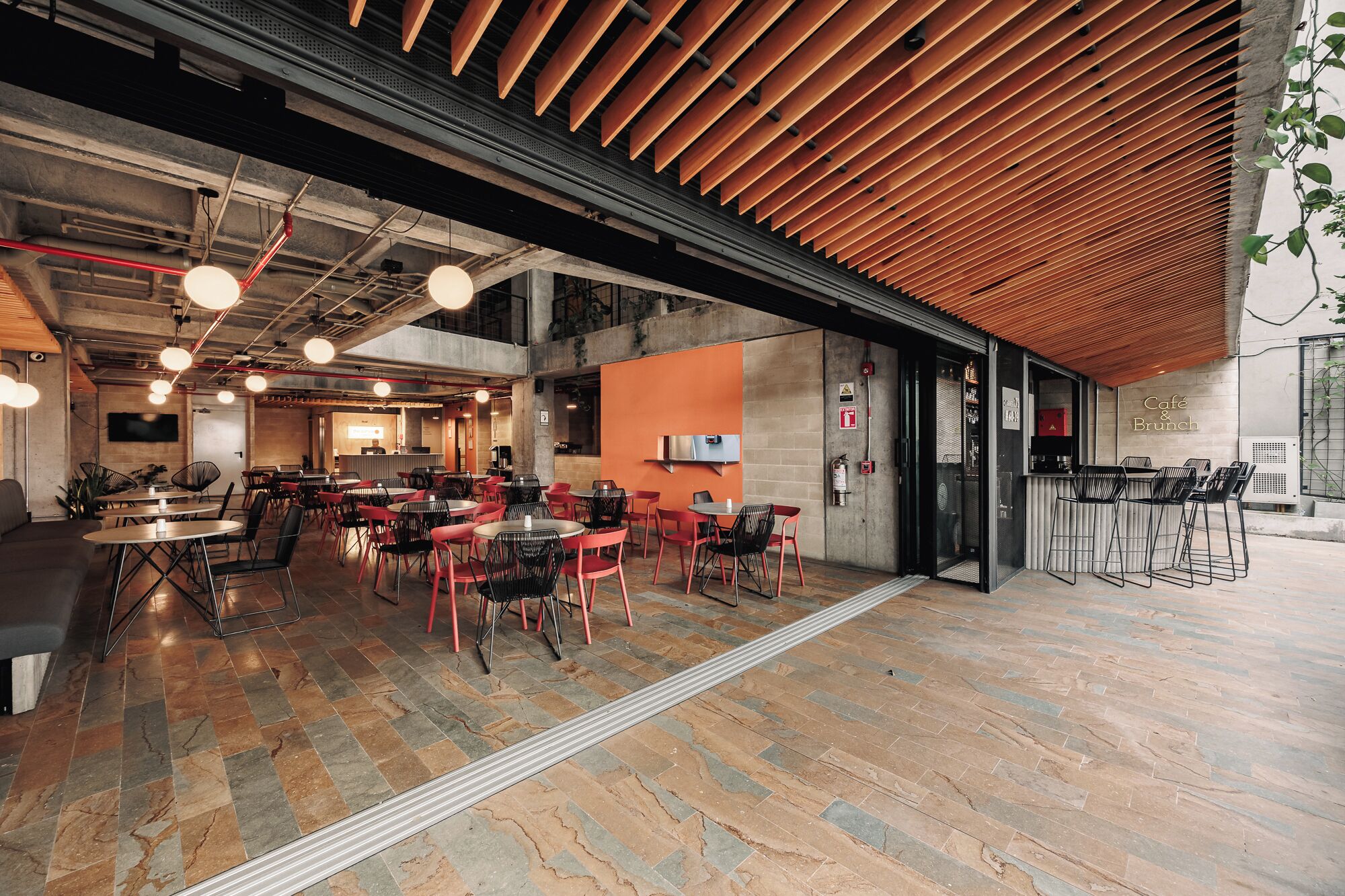 Un café moderne avec un aménagement intérieur comprenant plusieurs espaces de détente, une cuisine ouverte et un grand plafond en bois.