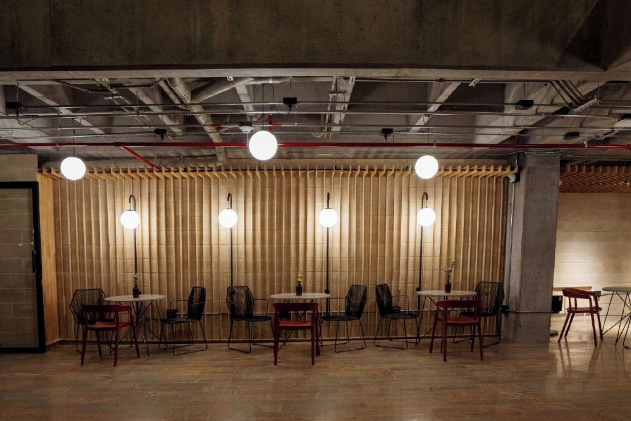 Un salón de conferencias con una larga mesa y sillas, un panel divisor de bambú y tuberías industriales en el techo.