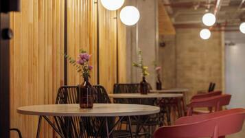 A restaurant interior with round tables, black metal chairs, and wooden panel walls.