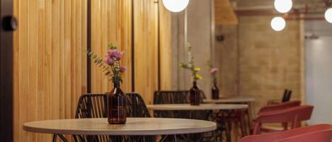 A restaurant interior with round tables, black metal chairs, and wooden panel walls.