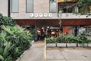 Un restaurante con diseño moderno, que presenta fachada de hormigón, techo de madera y una variedad de plantas de interior.