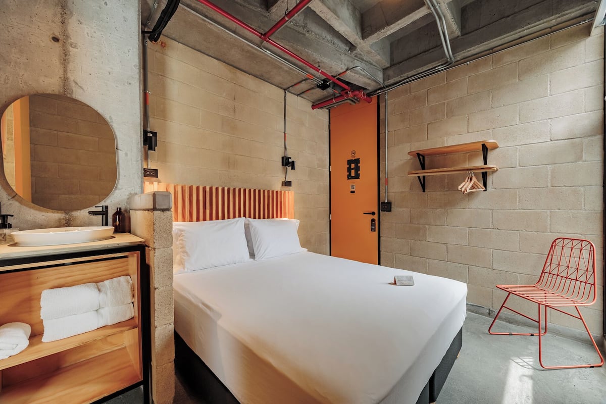 A modern hotel room with a large bed, a round mirror, a wooden vanity, and a red chair.