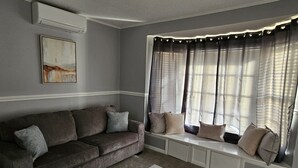 A living room with a grey sofa, a white coffee table, and a window with curtains. - Hidden Oasis (Martinez)