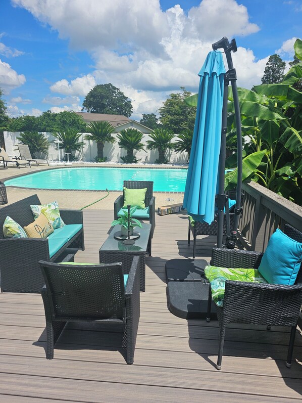 A deck with outdoor furniture, a pool, and a view of the surrounding greenery.