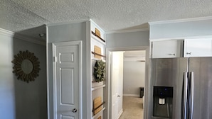 A kitchen with a stainless steel refrigerator, white cabinetry, and a decorative wall piece. - Hidden Oasis (Martinez)