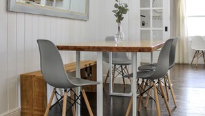 Un coin repas avec une table en bois, quatre chaises grises, un vase avec une plante et un grand miroir au mur.