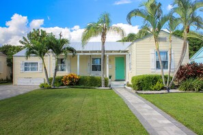 A single-story house with a green door, surrounded by a well-maintained lawn and palm trees. - A beautifully renovated private home with a large backyard, Pool, and Hot Tub (West Palm Beach)