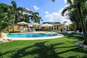 A backyard with a swimming pool, lounge chairs, and umbrellas. - A beautifully renovated private home with a large backyard, Pool, and Hot Tub (West Palm Beach)