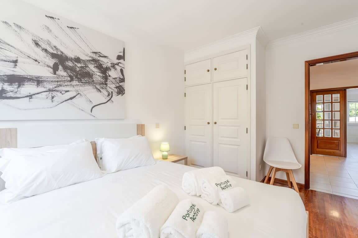 Habitación de hotel con una cama grande, un armario blanco, un cuadro en la pared y una puerta que da a otra habitación.