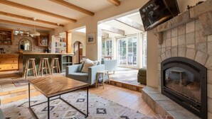 A spacious living room with a fireplace, a kitchen area with wooden beams, and a large window providing natural light. - Bright, Stylish, Equipped, Pet-Friendly, Great Location, Lake access, Ski lodge! (Truckee)