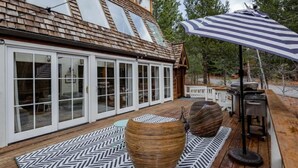 A wooden deck with a large umbrella, a woven basket, and a grill area. - Bright, Stylish, Equipped, Pet-Friendly, Great Location, Lake access, Ski lodge! (Truckee)