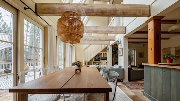 A spacious dining area with a wooden table and chairs, large windows, and a hanging light fixture. - Bright, Stylish, Equipped, Pet-Friendly, Great Location, Lake access, Ski lodge! (Truckee)