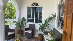 A covered patio area with wicker furniture, potted plants, and a stone-tiled floor.