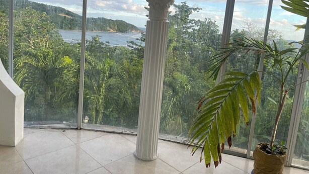 A room with large windows offering a view of a coastal landscape and dense greenery.