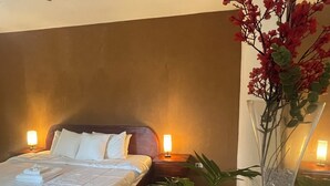 A hotel room with a bed, bedside lamps, a vase with flowers, and a potted plant.