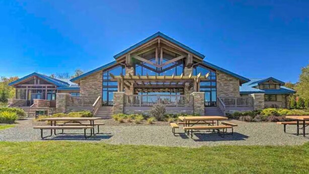En hytte med stenfacade, store vinduer og en overdækket terrasse med picnicborde.