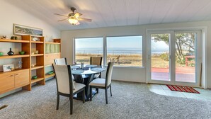 Un comedor con una mesa y sillas, un ventilador de techo y vistas a la playa a través de amplias ventanas.