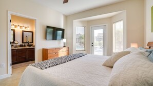 A bedroom with a large bed, a dresser, a vanity with lights, a ceiling fan, and a TV on the wall.