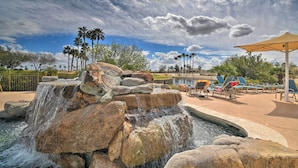 A water feature with cascading rocks and palm trees, surrounded by lounge chairs and a covered seating area.