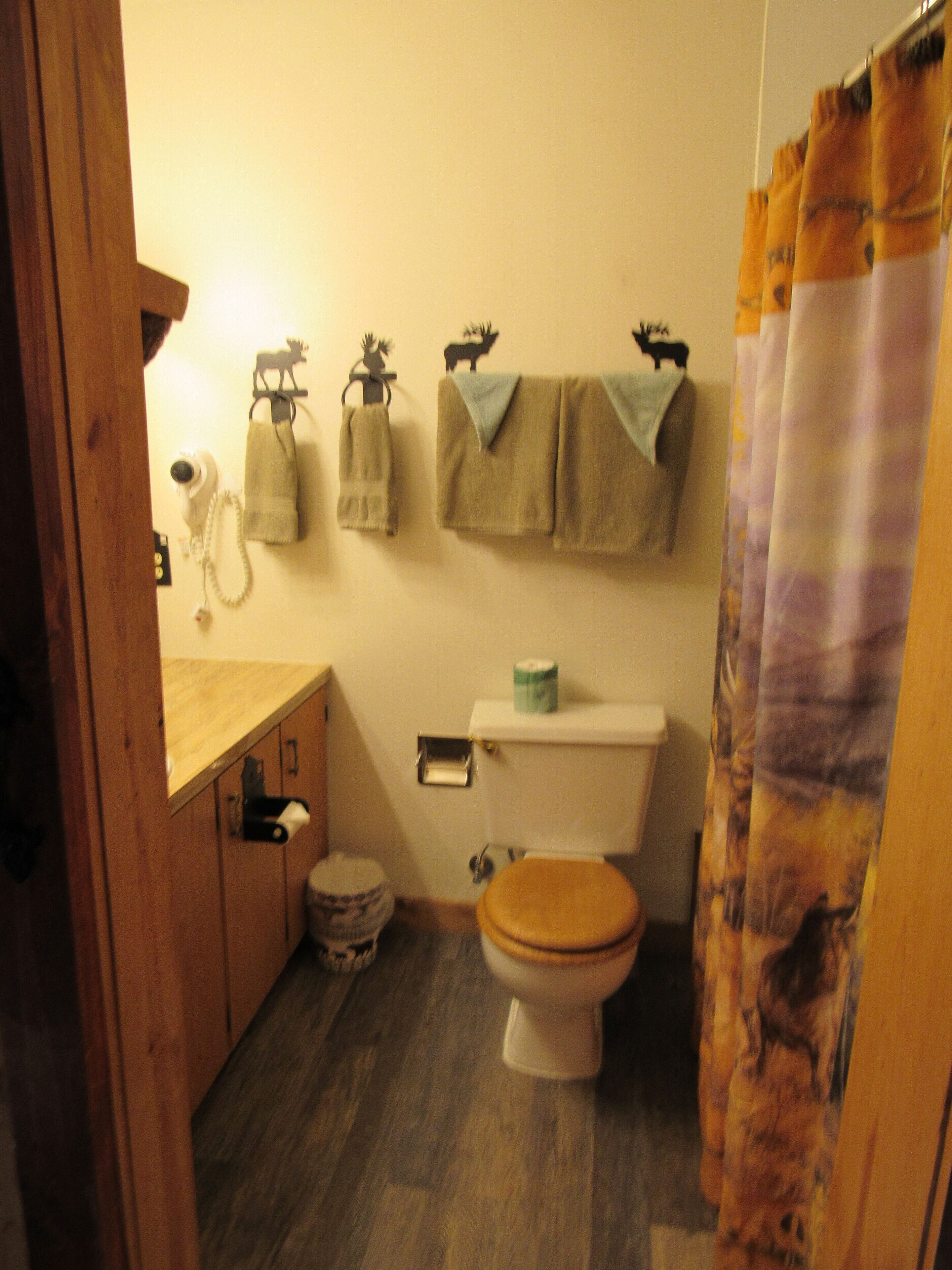 Un baño con suelo de madera, inodoro, lavabo con barra para toallas y cortina de ducha.