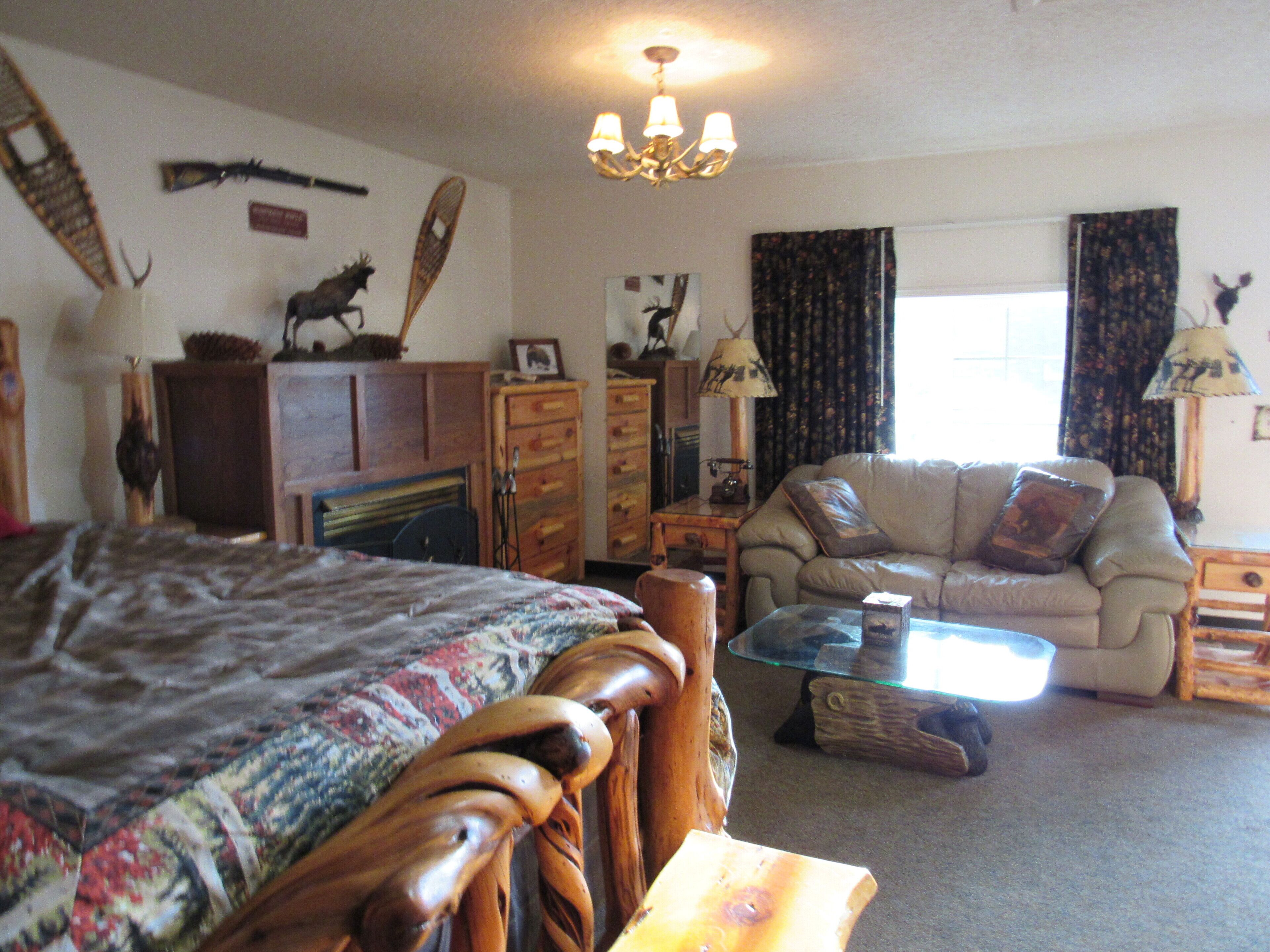 A cozy living room with a large bed, a sofa, a glass coffee table, and various decorative items.