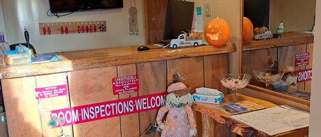 A room with a wooden desk, a clock, and a sign that reads "ROOM INSPECTIONS WELCOME".