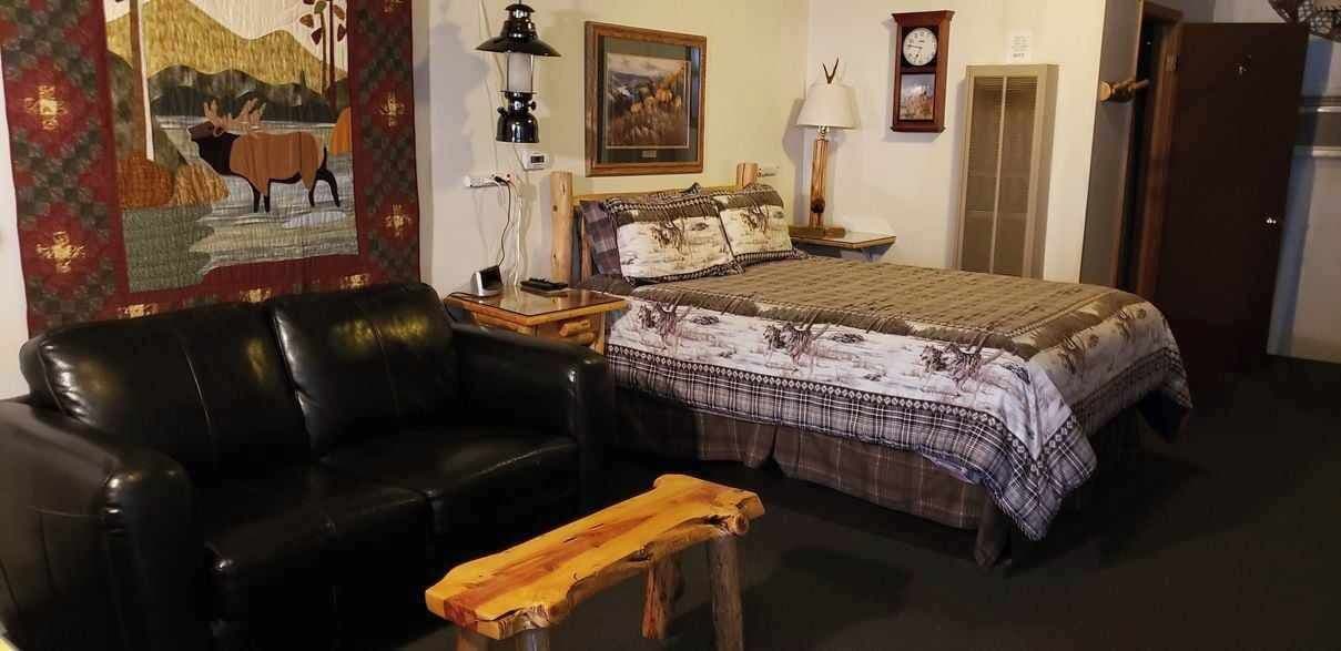 A room with a bed, a black leather sofa, a wooden bench, a wall clock, and a painting.